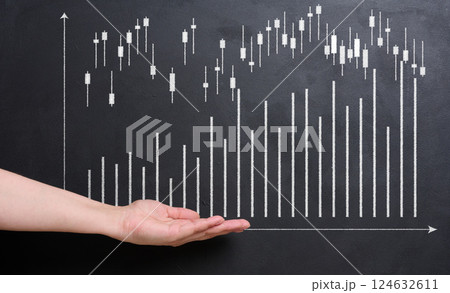A hand reaches out towards a stock market chart drawn in white on a black chalkboard. 124632611
