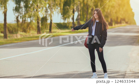 A young girl stands on the road and tries to stop any car. 124633344