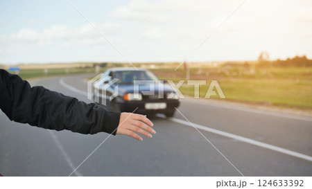 A young girl stands on the road and tries to stop any car. 124633392