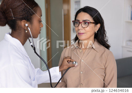 Young African cardiologist doctor examining mature Caucasian patient in office 124634016