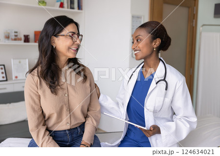 Happy supportive young African doc touching shoulder of senior woman 124634021