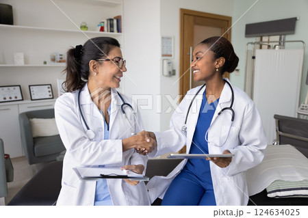 Happy diverse female docs shaking hands in hospital examination room Happy diverse female docs shaking hands in hospital examination room 124634025