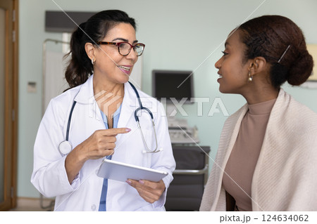 Positive Latin female doctor talking to young Black patient woman 124634062