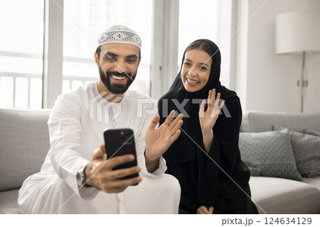 Happy Arabic couple greeting family using videocall app on smartphone 124634129