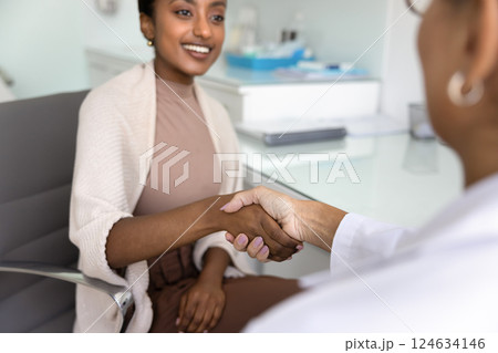 Positive young Black patient shaking hands with Caucasian doctor woman 124634146