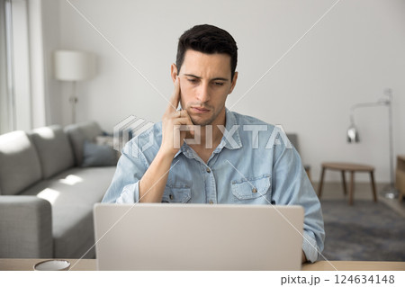 Young man deeply focused and thoughtful looks at laptop screen 124634148