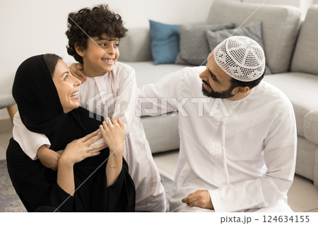Muslim couple with little 7s son cuddling seated on floor 124634155