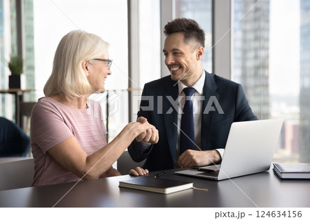 Happy older 55s businesswoman and young 35s businessman shaking hands 124634156
