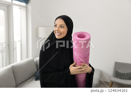 Happy Arabic woman dressed in abaya, holds rolled-up pink yoga Happy Arabic woman dressed in abaya, holds rolled-up pink yoga 124634161