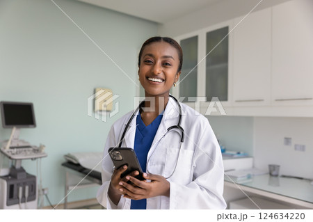 Happy beautiful African doctor woman holding smartphone 124634220
