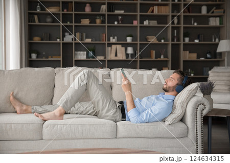 Millennial male relax on sofa with earphones connected to smartphone 124634315