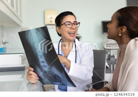 Cheerful Caucasian doctor and African patient woman discussing roentgen image Cheerful Caucasian doctor and African patient woman discussing roentgen image 124634319