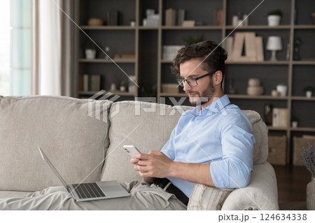 Relaxed millennial male spending time on cozy couch using gadgets Relaxed millennial male spending time on cozy couch using gadgets 124634338