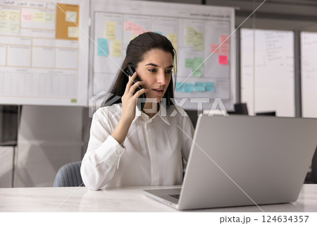 Serious busy young Latin project manager woman talking on cellphone Serious busy young Latin project manager woman talking on cellphone 124634357