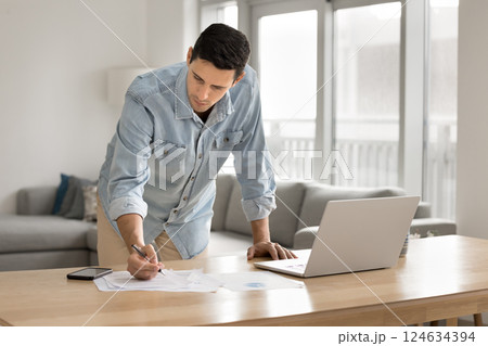 Man leaning over desk, making notes, focused on paperwork 124634394