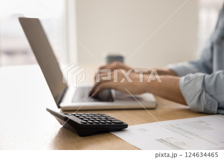 Man typing on laptop seated at table with calculator, closeup 124634465