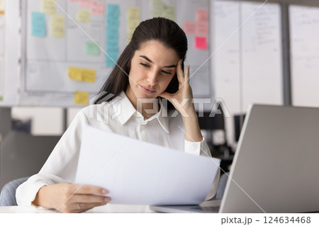 Thoughtful concerned Latin business professional woman reading financial document 124634468