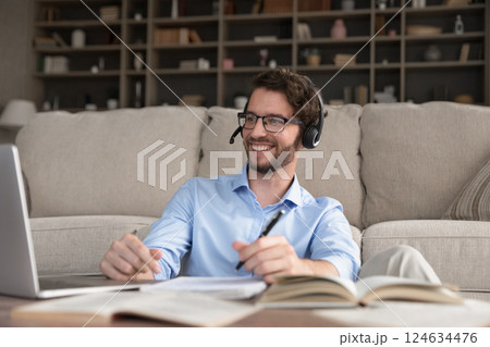 Cheerful young male student in earphones looking on notebook screen 124634476