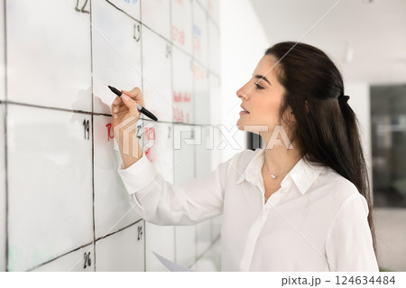 Positive confident young Hispanic businesswoman preparing presentation on whiteboard alone Positive confident young Hispanic businesswoman preparing presentation on whiteboard alone 124634484