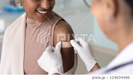 Female doctor sticking plaster on shoulder of patient Female doctor sticking plaster on shoulder of patient 124634486