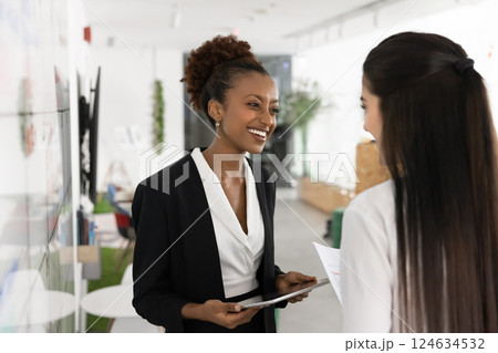 Cheerful young African business woman talking to female office friend Cheerful young African business woman talking to female office friend 124634532