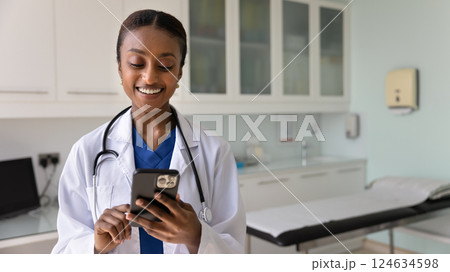 Cheerful young Black physician woman typing on mobile phone 124634598