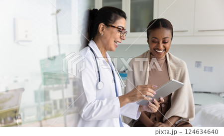 Happy practitioner and African patient watching examination report on tablet Happy practitioner and African patient watching examination report on tablet 124634640