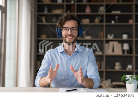 Happy young male in headset speaking at camera at workplace Happy young male in headset speaking at camera at workplace 124634679