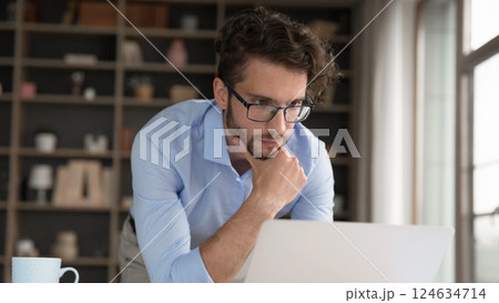 Pensive male stand by desk rub chin looking on notebook 124634714