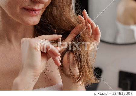 Smiling woman applying hair care capsule treatment to ends of damp hair, beauty and wellness concept, nourishing haircare routine in modern bathroom. 124635307
