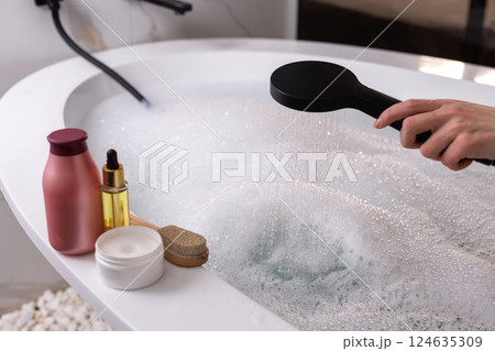 Woman filling bathtub with shower, luxury bubble bath preparation, relaxing spa skincare routine at home, wellness concept in modern bathroom setting. 124635309