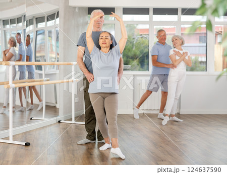 Elderly couple perform ballet pose with support during group training class in ballet hall 124637590