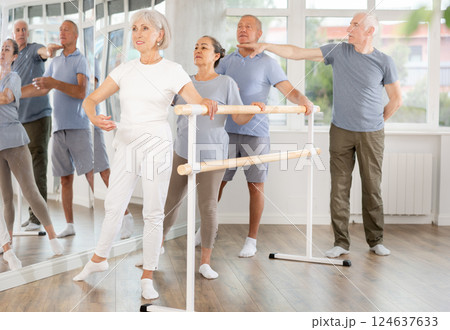Diligent mature men and women practicing basic positions with trainer standing by ballet 124637633