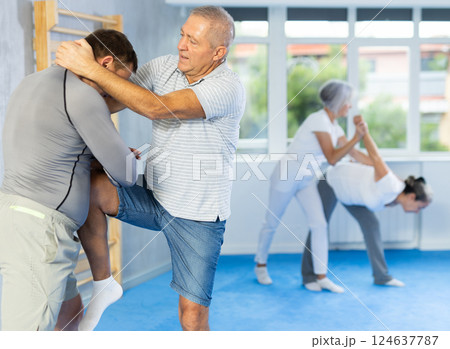Senior man in pair with middle-aged coach train Krav Maga and self-defense skills. 124637787