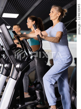 Elterly woman in sportswear doing cardio training on ellipsoid in gym Elterly woman in sportswear doing cardio training on ellipsoid in gym 124638045
