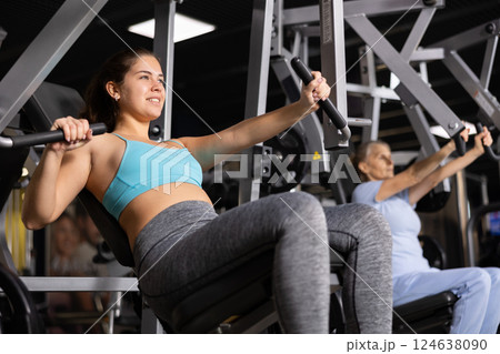 Young female training trains the muscles of the arms and press on simulator in gym. Sport concept Young female training trains the muscles of the arms and press on simulator in gym. Sport concept 124638090