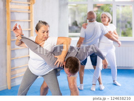 Senior woman in pair with middle-aged coach train Krav Maga and self-defense skills. 124638210