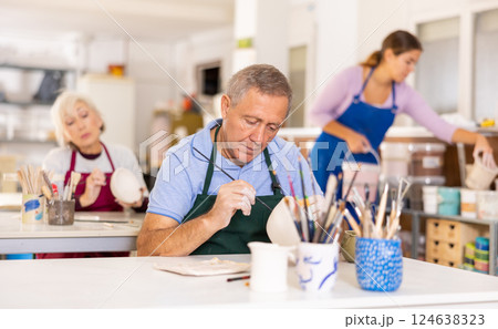 Mature craftsman painting clay plates acrylic paints in art studio Mature craftsman painting clay plates acrylic paints in art studio 124638323