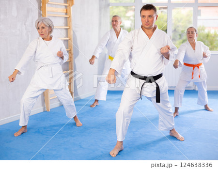 Elderly women and men in kimonos stand in a fighting stance during group karate training session Elderly women and men in kimonos stand in a fighting stance during group karate training session 124638336