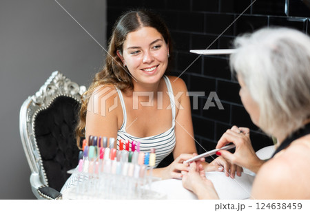 Girl client of beauty salon gave hand to blurry manicurist senior woman and enjoys having manicure Girl client of beauty salon gave hand to blurry manicurist senior woman and enjoys having manicure 124638459
