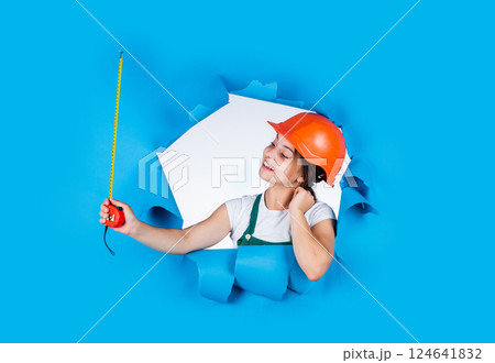 teen girl builder in protective helmet use tape measuer, size 124641832