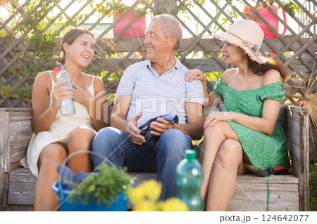 Woman in straw hat is sitting on wooden bench and chatting sweetly with sister and senior father Woman in straw hat is sitting on wooden bench and chatting sweetly with sister and senior father 124642077