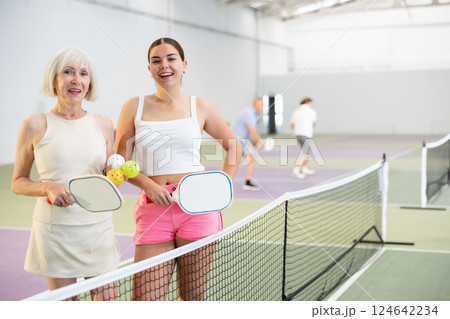 Smiling women with racquets and balls standing in pickleball court and looking at camera 124642234