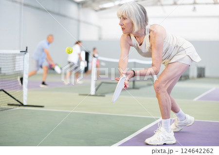 Sporty senior woman playing pickleball on indoor court Sporty senior woman playing pickleball on indoor court 124642262