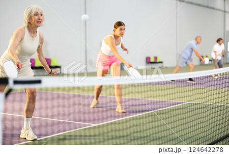 Senior woman playing doubles pickleball with young female partner 124642278