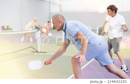 Two athletic men of different ages are playing a game of pickleball on a court inside sports facility 124642283