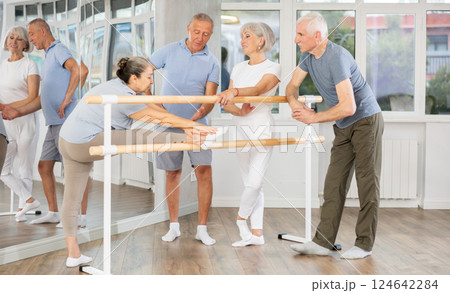 Group of cheerful relaxed aged people talking and stretching beside ballet barre during training at ballet school 124642284