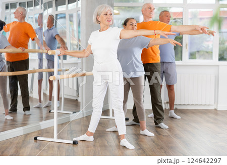 Mature woman in sportswear participating 2nd position of ballet stance at barre with group in choreography studio 124642297