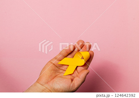 Raising awareness for cancer with a yellow ribbon on a pink background Raising awareness for cancer with a yellow ribbon on a pink background 124642392