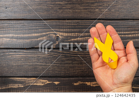 Holding a yellow ribbon symbolizing cancer awareness and support for survivors Holding a yellow ribbon symbolizing cancer awareness and support for survivors 124642435